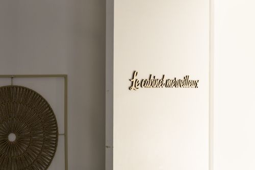 Lettrage en bois « Le cabinet merveilleux » sur le mur, à côté d'un cadre en rotin