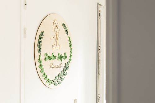 Enseigne en bois « Studio Anjali — Namasté » accrochée à la porte du studio