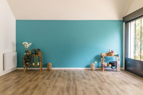 Salle de pratique vue dans sa largeur, grand mur bleu, parquet clair et baie vitrée