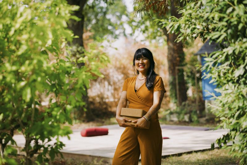 Amphay Tran dans le jardin du studio L'Instant Présent, briques de yoga à la main